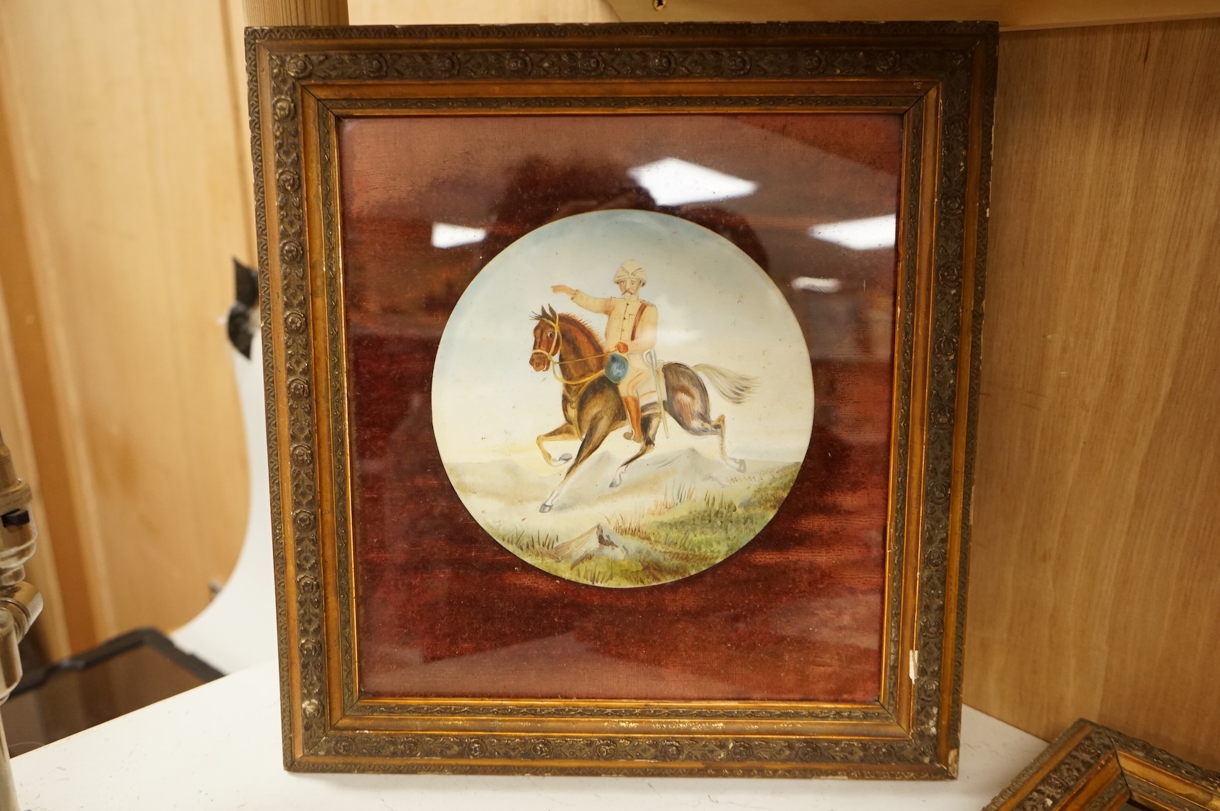 A pair of naive watercolours on circular porcelain panels, soldiers on horseback, framed, 15cm in diameter